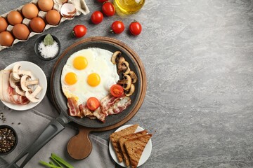 Tasty fried eggs with bacon and mushrooms served on grey table, flat lay. Space for text