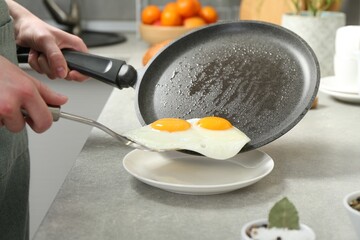 Woman putting tasty fried eggs onto plate from frying pan in kitchen, closeup