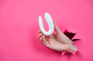 Female hand sticking out with white sex toy through pink paper background. Copy space. 