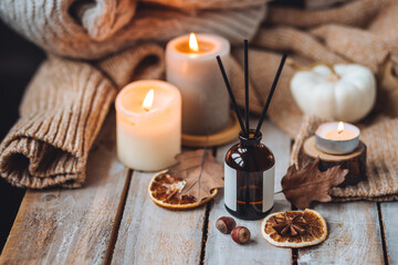 Concept of cozy fall home atmosphere, aromatherapy. Perfume, apartment aroma diffuser with autumn scent of pumpkin spicy sweet pie, cinnamon, anise. Room decor with pumpkins, dry orange, wool plaid