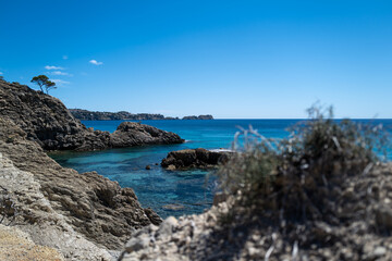 Secluded rocky cove with crystal-clear turquoise water under a vibrant blue sky, showcasing a tranquil seascape.