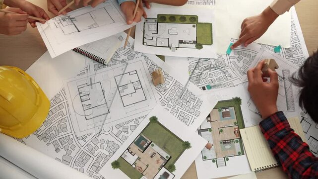 Architect and safety engineer discussion about building construction use blueprint on table with architectural document, measurement tool and wooden block scatter around at modern office. Delineation.
