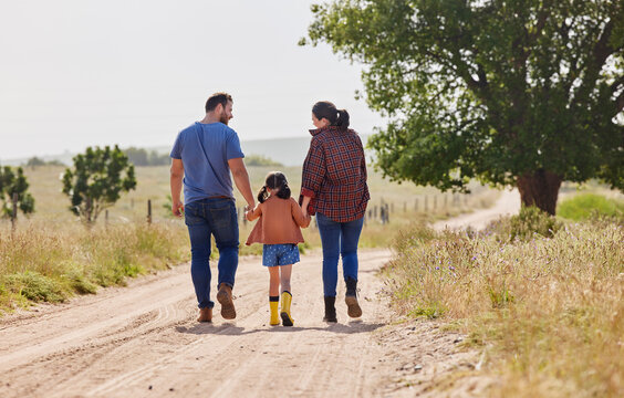 Holding hands, parents and walking with kid on farm for love, care and support with family on dirt road. Back, mother and father with girl in countryside to travel together, holiday and agriculture - Powered by Adobe
