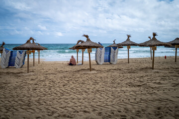 A lone man sits on a tranquil beach, enjoying the calm ocean waves under a partly cloudy sky.