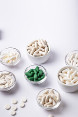 Dietary supplements, vitamins and minerals in small plates on white background. Happy and healthy lifestyle. Thite and green tablets. Top view.