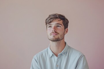 Fototapeta premium Thoughtful Young Man in Casual Attire Against a Soft Pink Background