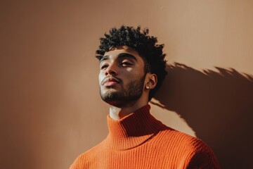 Fototapeta premium Stylish Young Man in Orange Sweater Posing Against a Warm Background