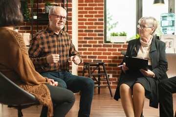 Caucasian old man shares his struggles as senior female psychologist attentively listens and takes notes. Retired male person speaking about his addiction recovery process during group therapy session