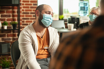 Closeup on caucasian guy with face mask, speaking about his anxiety at rehab counseling program....