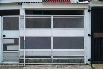 A contemporary white sliding gate with a mesh design, situated next to a black gate. The image...