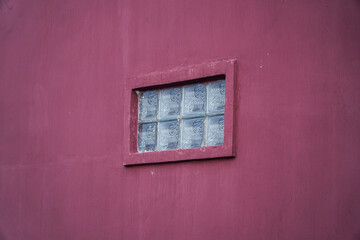 A small, square window with glass blocks set into a maroon wall. A Small Glass Block Window on a Maroon Wall