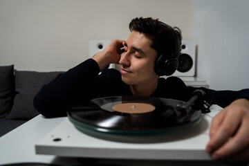 Cheerful hipster is listening to music by vintage vinyl records and feeling real emotions of music lover. Emotional music lover is listening a vinyl record on a turntable player.