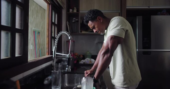 Man leaning on kitchen sink gazing out window, lost in thought, quiet moment of reflection, deep contemplation, personal introspection, solitude, domestic environment