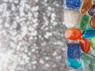 A collection of colorful stones and crystals are displayed on a glass surface. Bokeh background...
