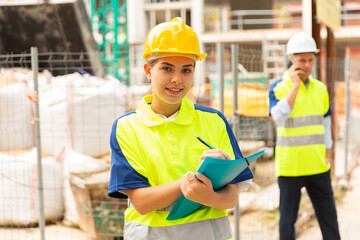 Portrait of a young confident female process engineer writing work notes on a tablet while standing on a construction site
