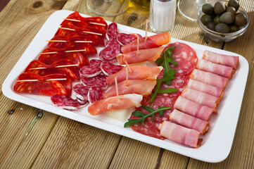 Appetizing cold cuts from Spanish ham, spicy dry-cured sausages and bacon with olives and arugula on white plate
