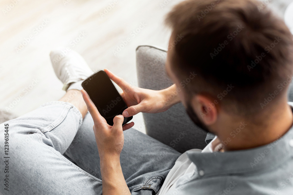 Poster above view of young guy using smartphone with blank screen at home, mockup for mobile app design. mi