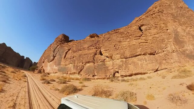 Off road vehicle navigating a dirt road through towering sandstone formations in Alula Sharaan Nature Reserve in Saudi Arabia. Capturing spirit of adventure in a stunning desert landscape. Aerial view