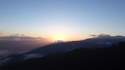 Fototapeta premium Sunrise over mountain range layers hills valleys mist clouds serene tranquil atmosphere pastel colors sky warm light illuminating landscape ideal nature travel enthusiasts