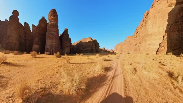 Off road vehicle navigating a dirt road through towering sandstone formations in the Alula Sharaan Nature Reserve, capturing the spirit of adventure in a stunning desert of Saudi Arabia. Aerial view