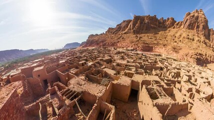 Panoramic aerial view of the ancient mud brick ruins of Alula Old Town and the imposing Alula Fort, standing as testaments to the region's rich history under a clear blue sky in Saudi Arabia