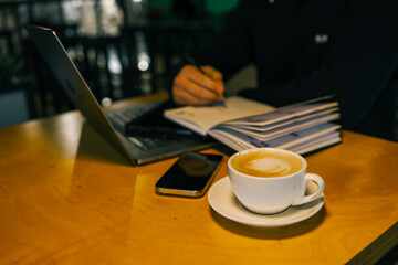 A professional workspace with a person organizing tasks using a notebook, tablet, and laptop on a wooden table, creating a productive and modern office environment