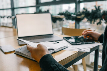 A professional workspace with a person organizing tasks using a notebook, tablet, and laptop on a wooden table, creating a productive and modern office environment