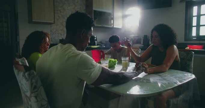Family holding hands in prayer before meal, father, mother, son, and daughter expressing gratitude, faith, and unity at dining table, spiritual tradition in home setting