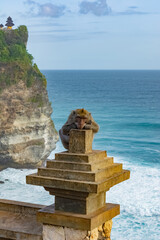 A monkey in Uluwatu Monkey Forest, Badung, Bali. Uluwatu Temple is visible in the background.
