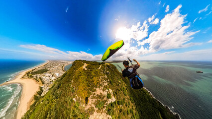 Extreme paragliding pilot soaring in the New Zealand beach at sunset. Adventure concept