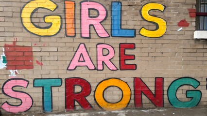 Colorful graffiti with bold text 'GIRLS ARE STRONG' painted on a brick wall. Feminist street art and empowerment message