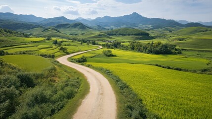Winding Dirt Road Through Lush Green And Yellow Fields Leading To Distant Mountains
