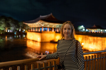 Night in Korea: Woman admires the illuminated Gyeongbokgung Palace across a tranquil pond.