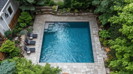 A pool with a stone border and a patio area with a few lounge chairs