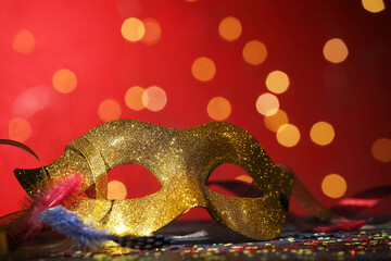 Beautiful carnival mask and confetti on color background with blurred lights, closeup