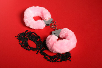 Pink fluffy handcuffs and lace mask on red background