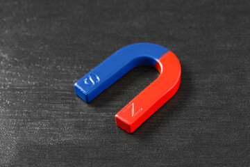 One horseshoe magnet on black wooden table, closeup