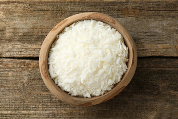 White soy wax flakes in bowl on wooden table, top view