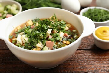 Delicious okroshka soup and ingredients on wooden table, closeup