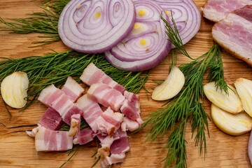 Sliced ​​pork bacon with onion rings, finely chopped lard, garlic and dill on a wooden board.