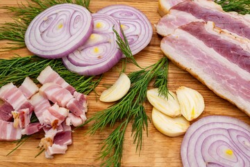 Sliced ​​pork bacon with onion rings, finely chopped lard, garlic and dill on a wooden board.