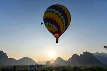 A vibrant hot air balloon floats serenely over a sun-kissed mountain range, creating an...