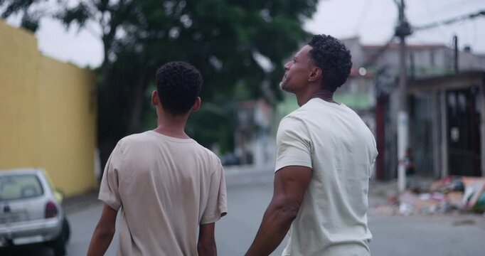 Rear view of father of African descent with arm around teenage son, walking together in a quiet urban neighborhood, sharing a moment of connection and trust