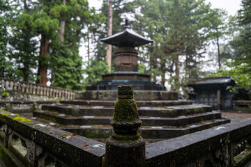 Fototapeta premium A moss-covered stone pagoda stands serene in a mystical Japanese forest, rain gently falling.