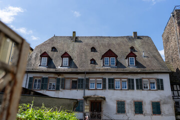 A charming, aged European house with a slate roof and numerous windows stands in a picturesque town setting.