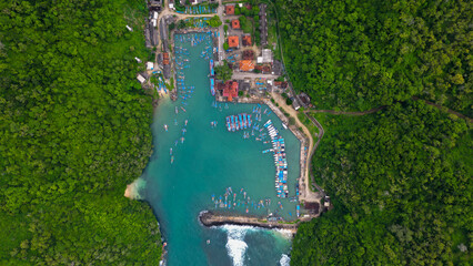 A breathtaking view of Sadeng Beach Pier, where dozens of fishing boats dock along the harbor, blending beautifully with green mountains and the vast blue ocean.
