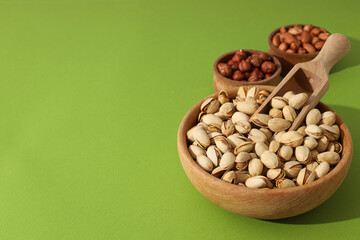 Different types of nuts in wooden bowls on a green background