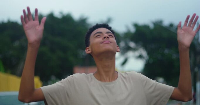 Teenage boy raising hands in gratitude, looking up with faith and embracing the presence of God, radiating spirituality, hope, and positivity in a serene outdoor environment