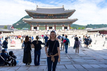 Obraz premium A woman stands in front of Gyeongbokgung Palace in Seoul, South Korea, enjoying the beautiful day and the historical landmark.