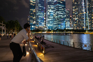 Fototapeta premium Businessman on a call at night, overlooking a stunning cityscape of skyscrapers and calm waters.